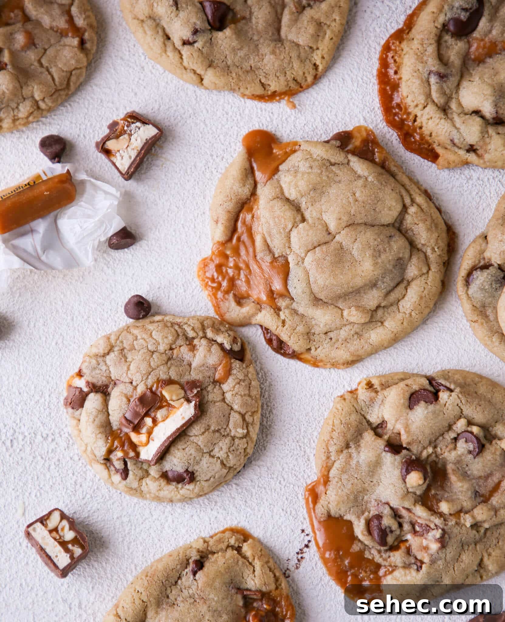 Brown Butter Snickers Cookies Stuffed With Caramel 2 Caramel Stuffed Brown Butter Snickers Chocolate Chip Cookies arranged on white surface