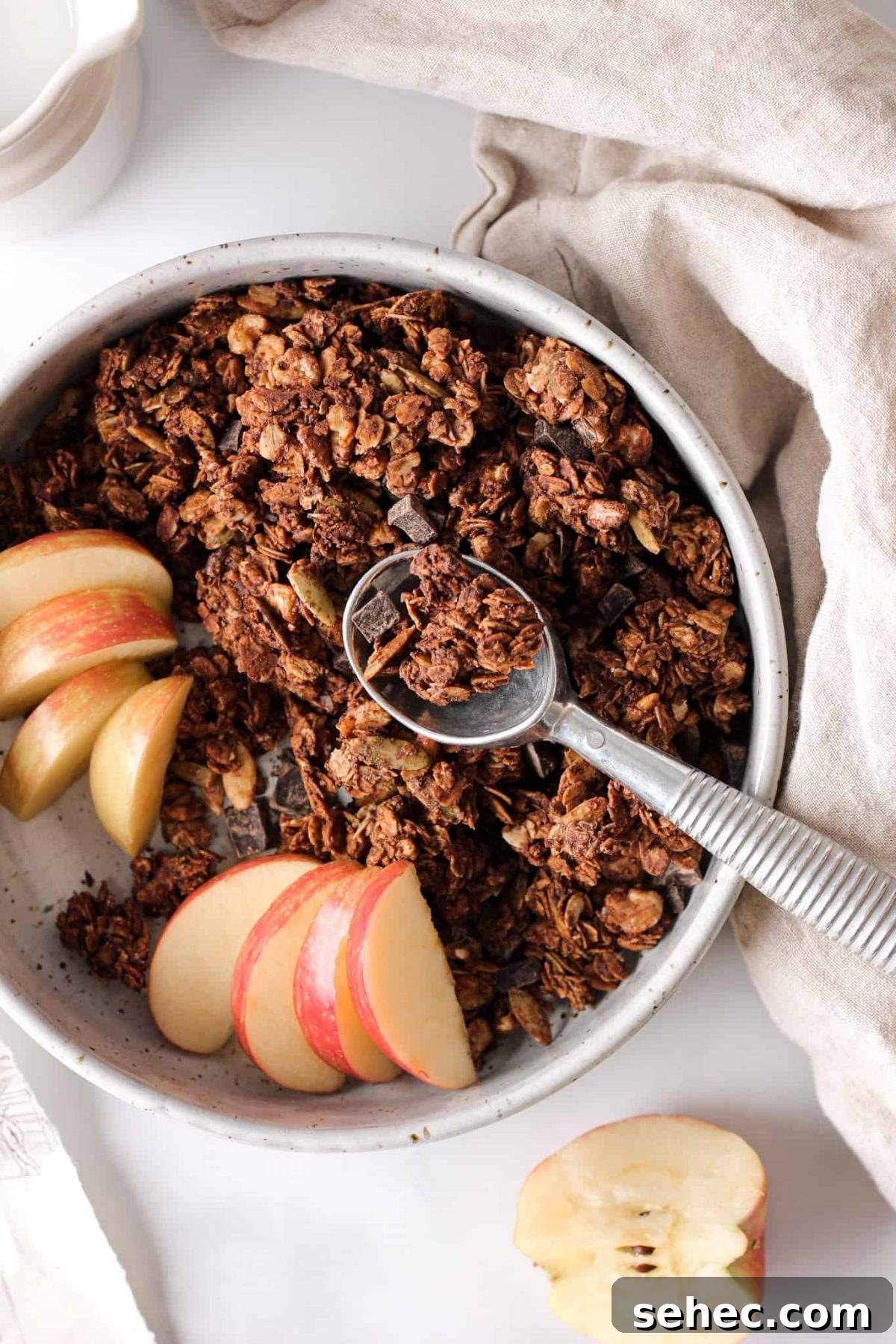 Healthy Chocolate Granola a bowl of chocolate chunk granola with a spoon and sliced apples for baking blog