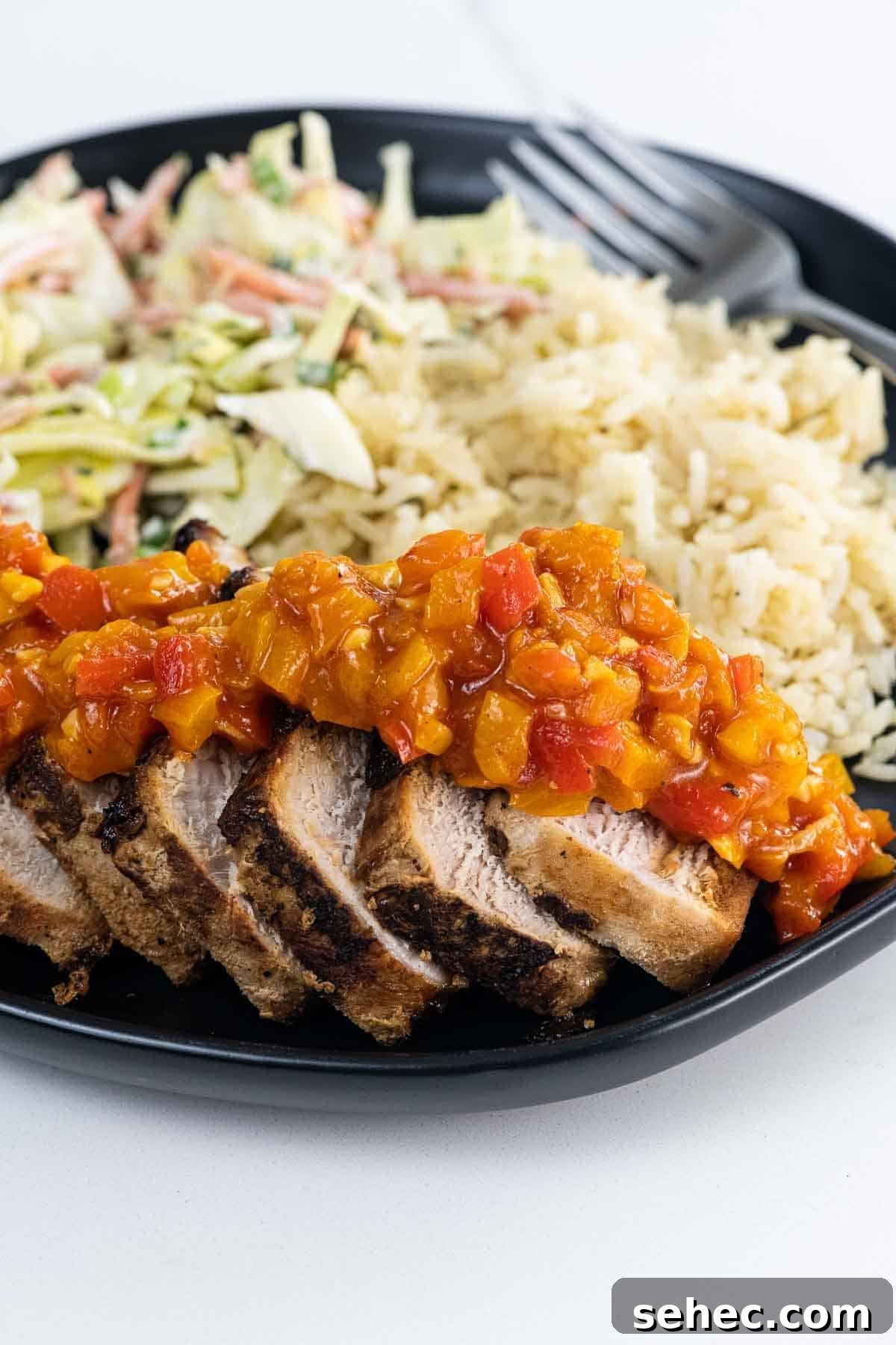 bell pepper sauce over sliced pork on a plate with rice and coleslaw