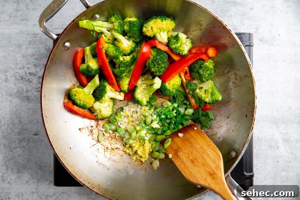 Stir Fry Recipe with Any Vegetables and Meat 7 Process shot showing garlic, ginger and scallions going into a stir fry in a work.