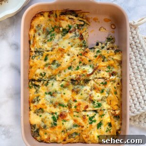 Marry Me Chicken Pasta Bake with Creamy Tuscan Sauce 12 A Marry Me Chicken Pasta Bake casserole topped with melted cheese and garnished with fresh herbs sits in a rectangular dish on a marble countertop. A portion has been served on a nearby plate, revealing the dish's textured and creamy interior.