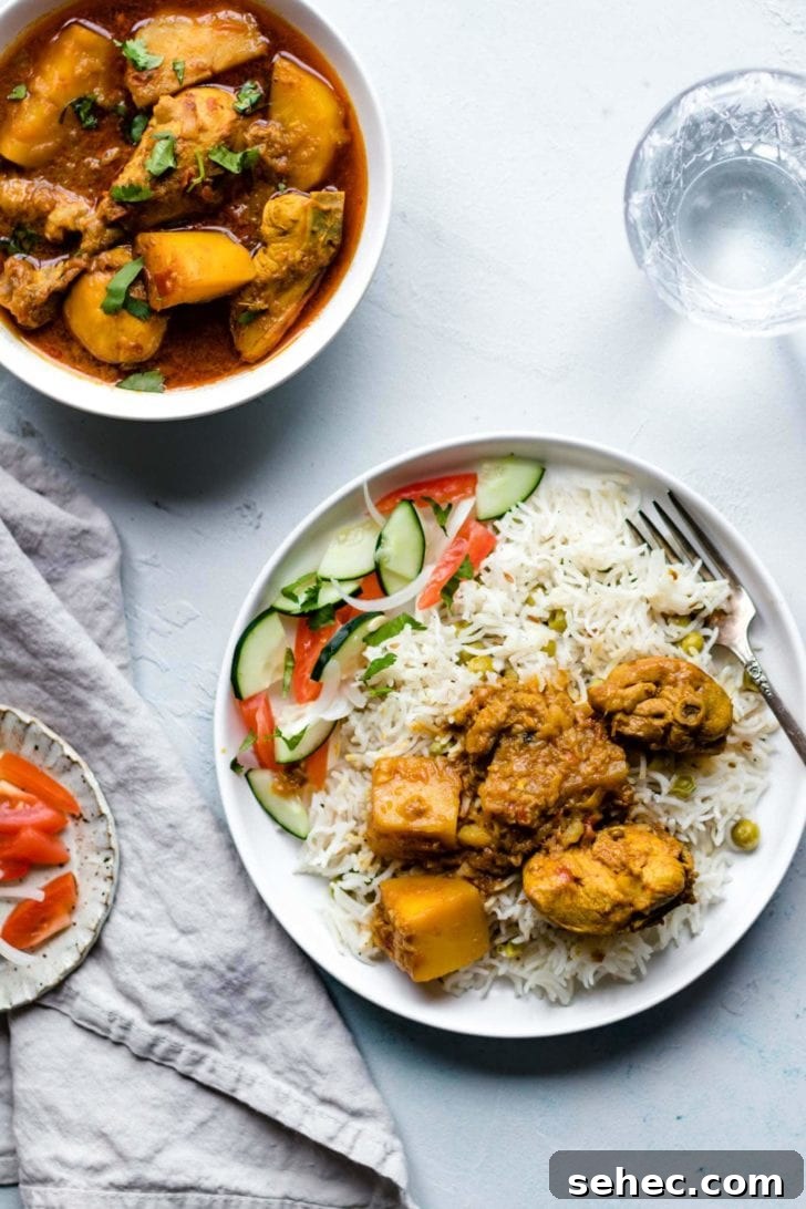 Instant Pot Chicken Curry Recipe 11 Chicken Curry with potatoes on a plate with rice and vegetables with a glass of water on the side