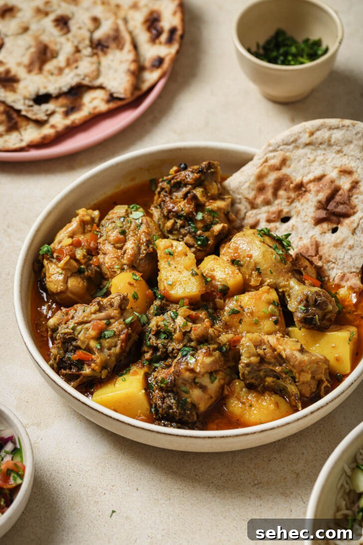 Instant Pot Chicken Curry Recipe 9 Close up of a bowl of Pakistani Chicken Curry garnished with cilantro and garam masala with a piece of naan on the side.