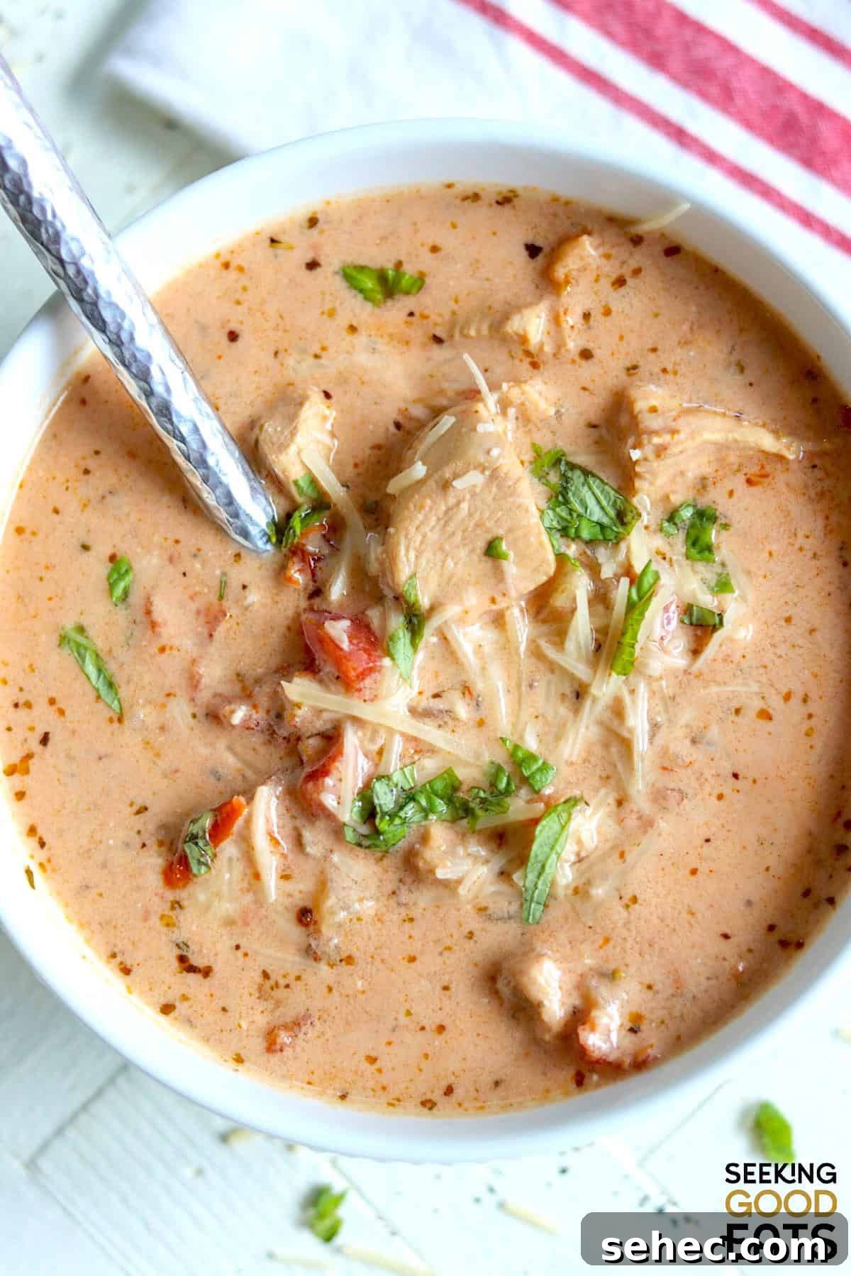 A round white bowl of creamy sun-dried tomato chicken soup garnished with parmesan