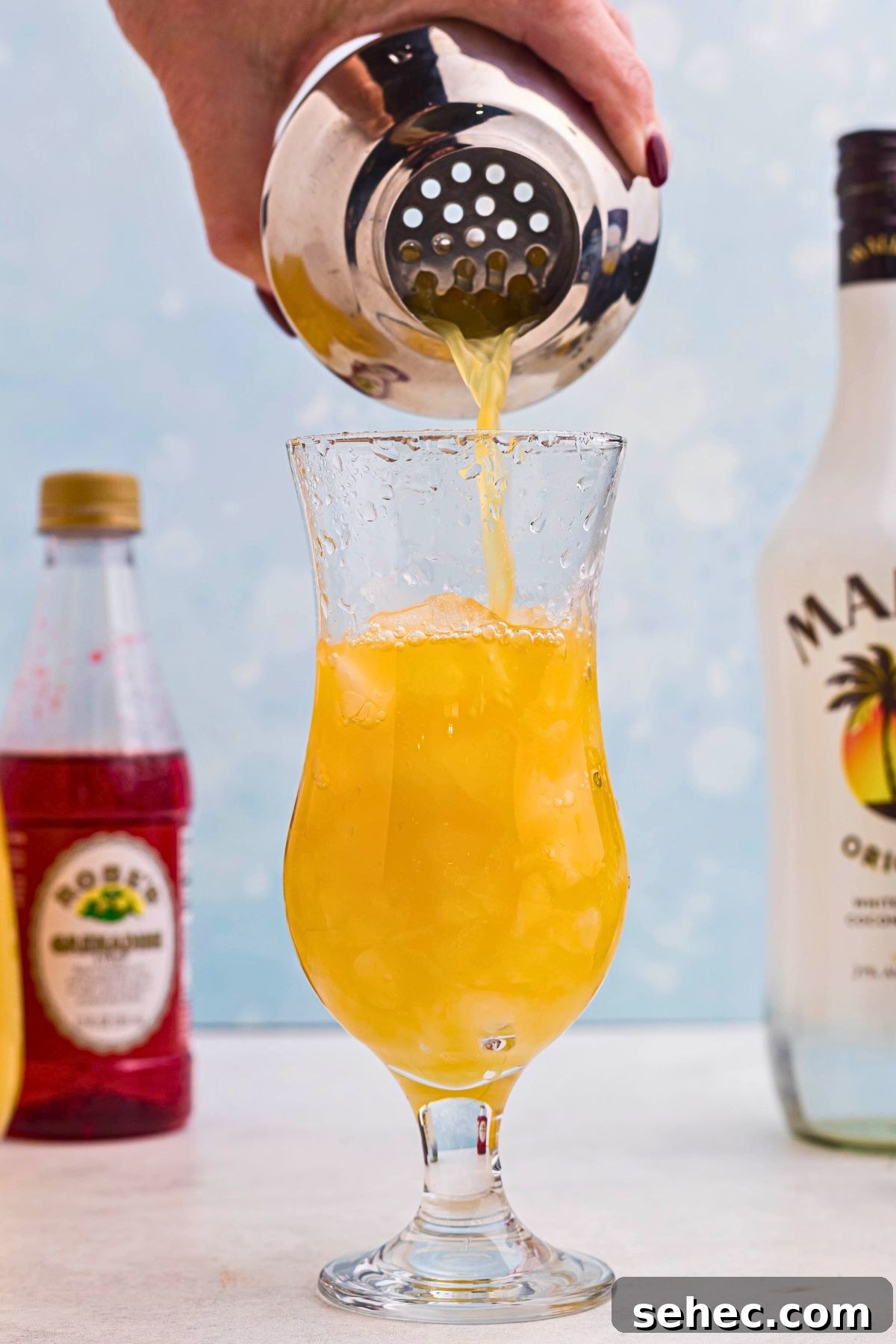 Bahama Mama Cocktail Recipe 5 Orange Bahama Mama cocktail being poured from a shaker into a hurricane glass over ice.