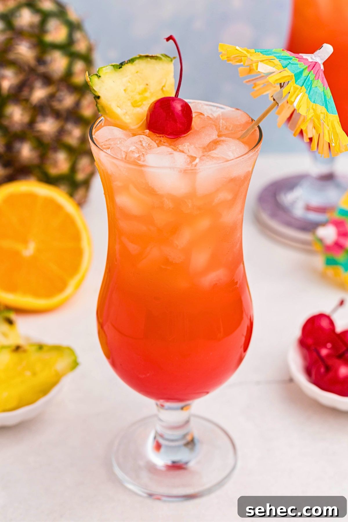 Bahama Mama Cocktail Recipe 8 Red and orange Bahama Mama cocktail in a hurricane glass with orange slices, cherries, and a paper umbrella on a marble table.