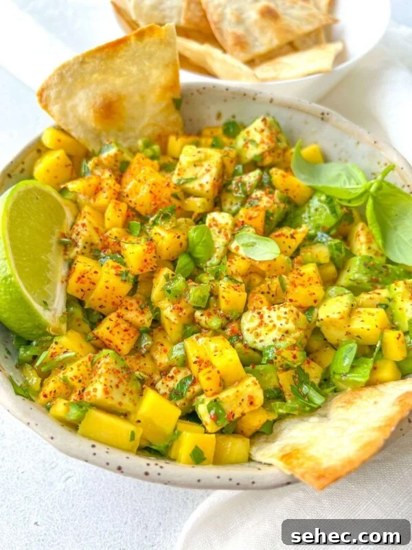 A bowl of vibrant mango avocado salsa, crafted from a delicious Mango Salsa Recipe, garnished with chili powder, fresh herbs, and a lime wedge, served alongside crispy tortilla chips.