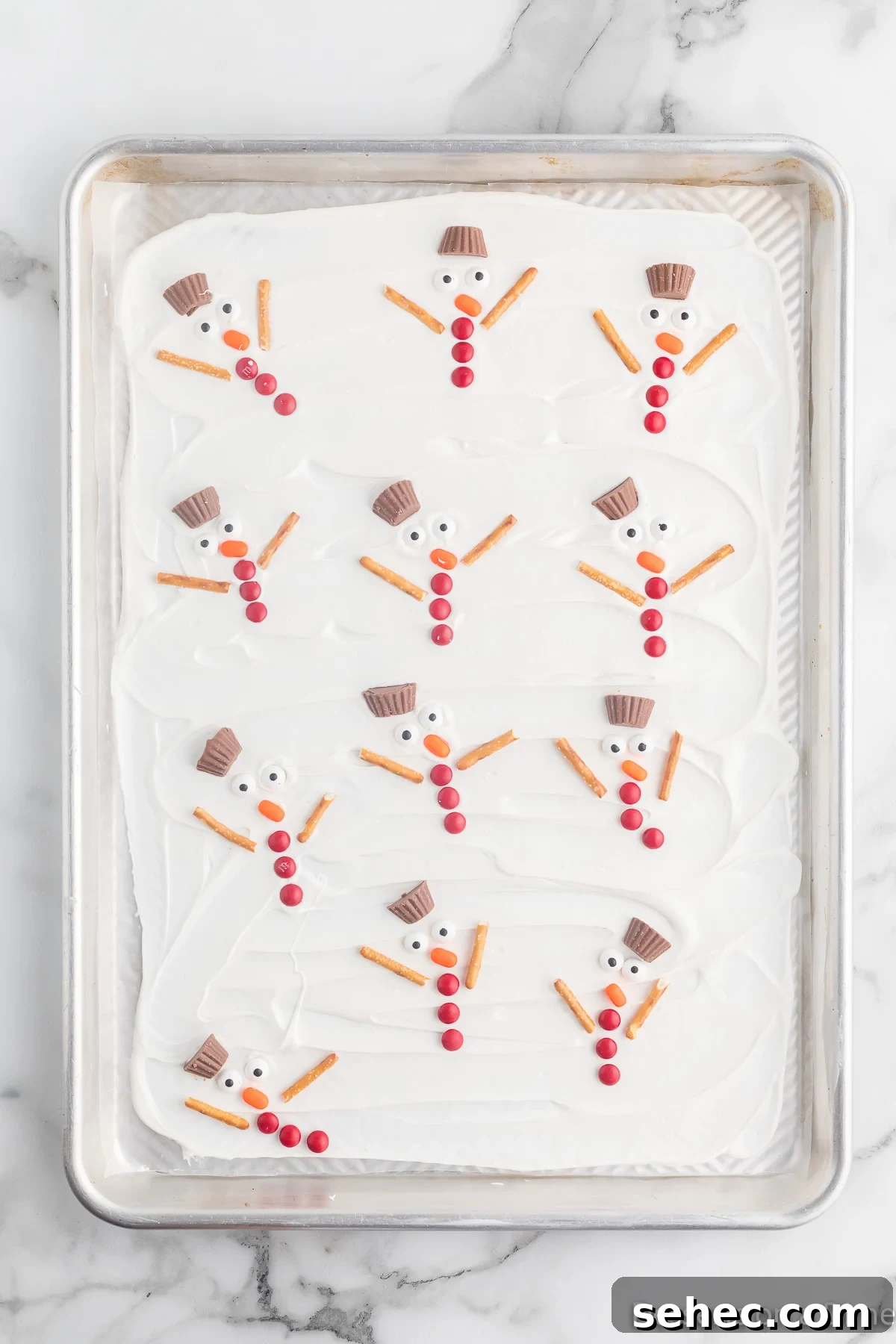 Melted Snowman Chocolate Bark Recipe 9 Baking sheet with snowmen arranged all over the chocolate.