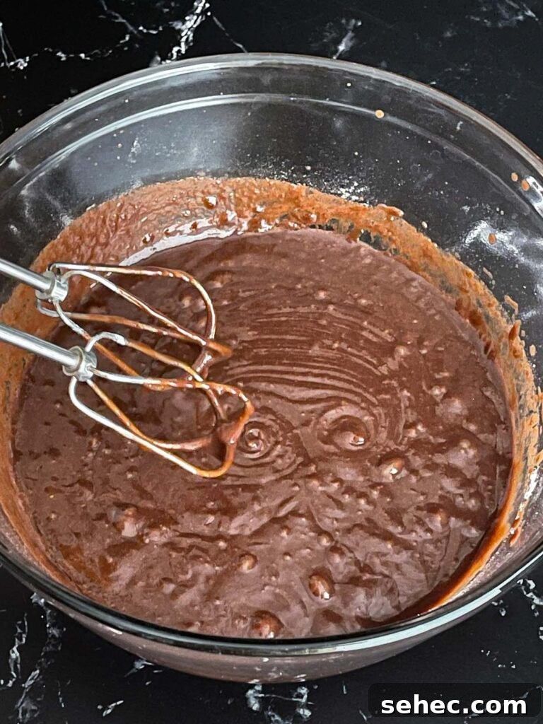 Buttermilk brownie batter mixed in a large glass bowl on a dark surface.