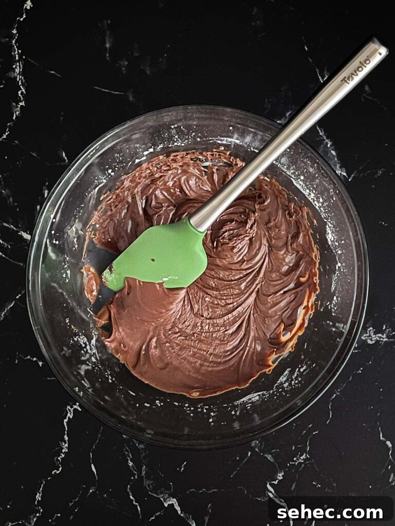 Buttermilk chocolate icing mixed in a large glass bowl on a dark surface.