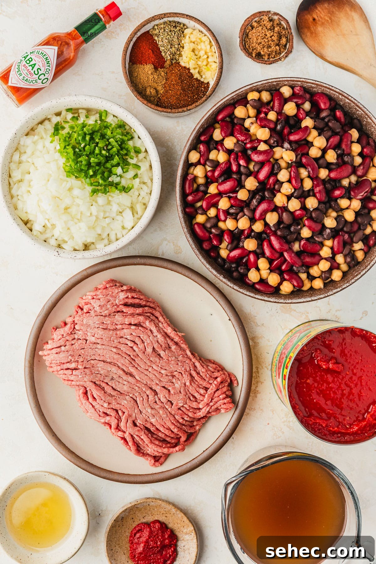 Chili Charcuterie Board with Homemade Chili Recipe 3 Brown and white bowls of beans, meat, veggies, tomato paste, oil, beef broth, spices, and tomato sauce on a white counter.