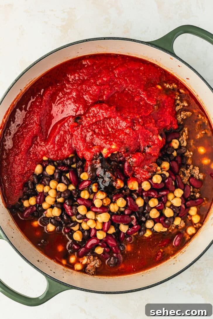 Chili Charcuterie Board with Homemade Chili Recipe 8 Ingredients for three bean chili in a green Dutch oven on a white counter.