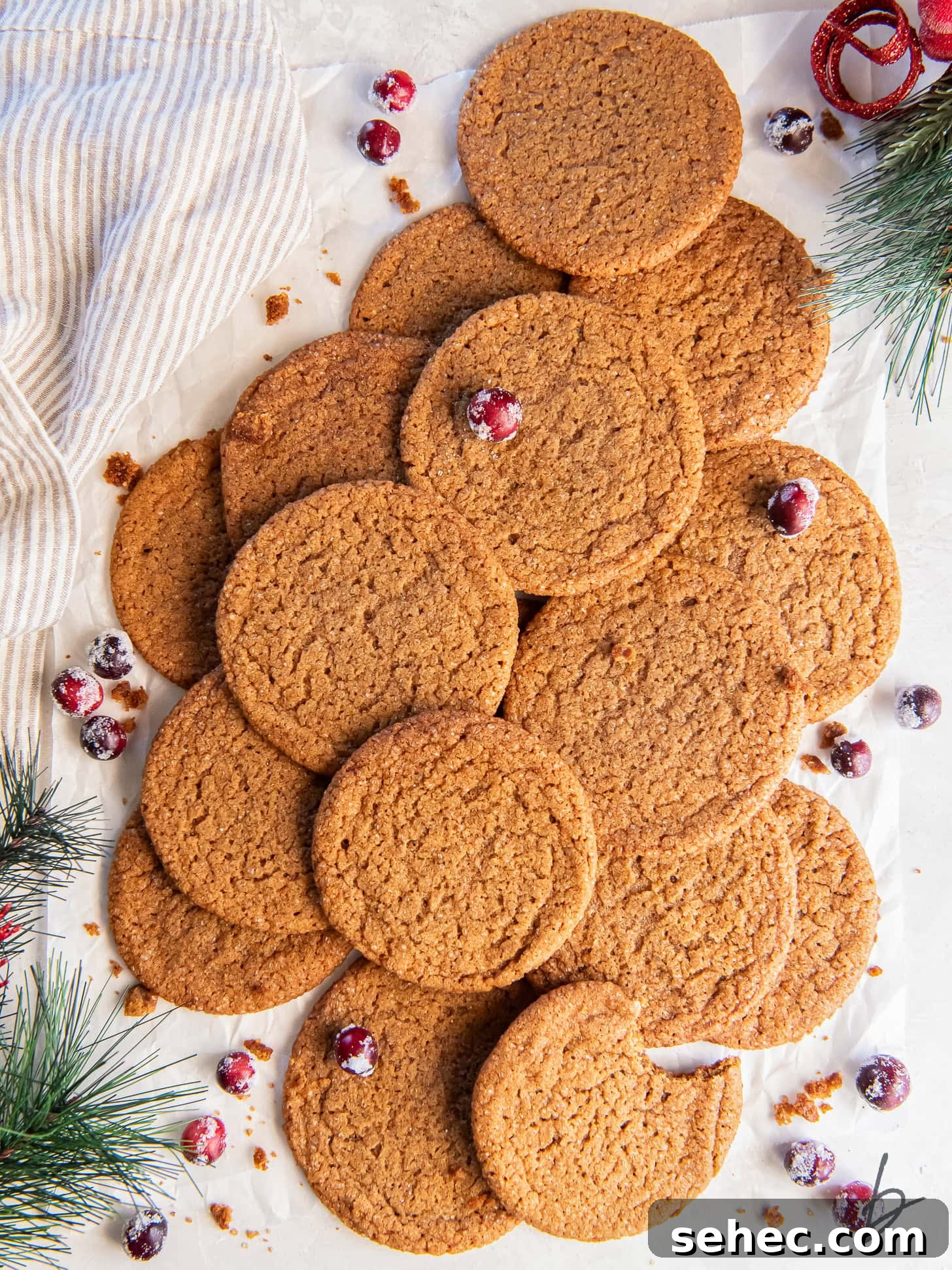 Thin and Crispy Gingersnap Cookies 5 pile of gingersnap cookies on tabletop with some sugared cranberries and faux greenery.