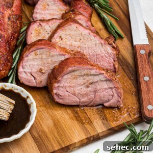 Juicy Smoked Pork Tenderloin Recipe 11 Juicy tenderloin cut into slices on a cutting board with a knife and fork, and fresh rosemary.