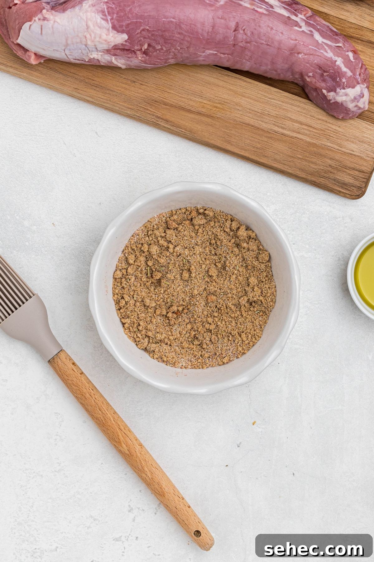 Juicy Smoked Pork Tenderloin Recipe 5 Seasonings and brown sugar in a small white bowl, mixed together, on a white marble table, before being added to the pork tenderloins and smoked.