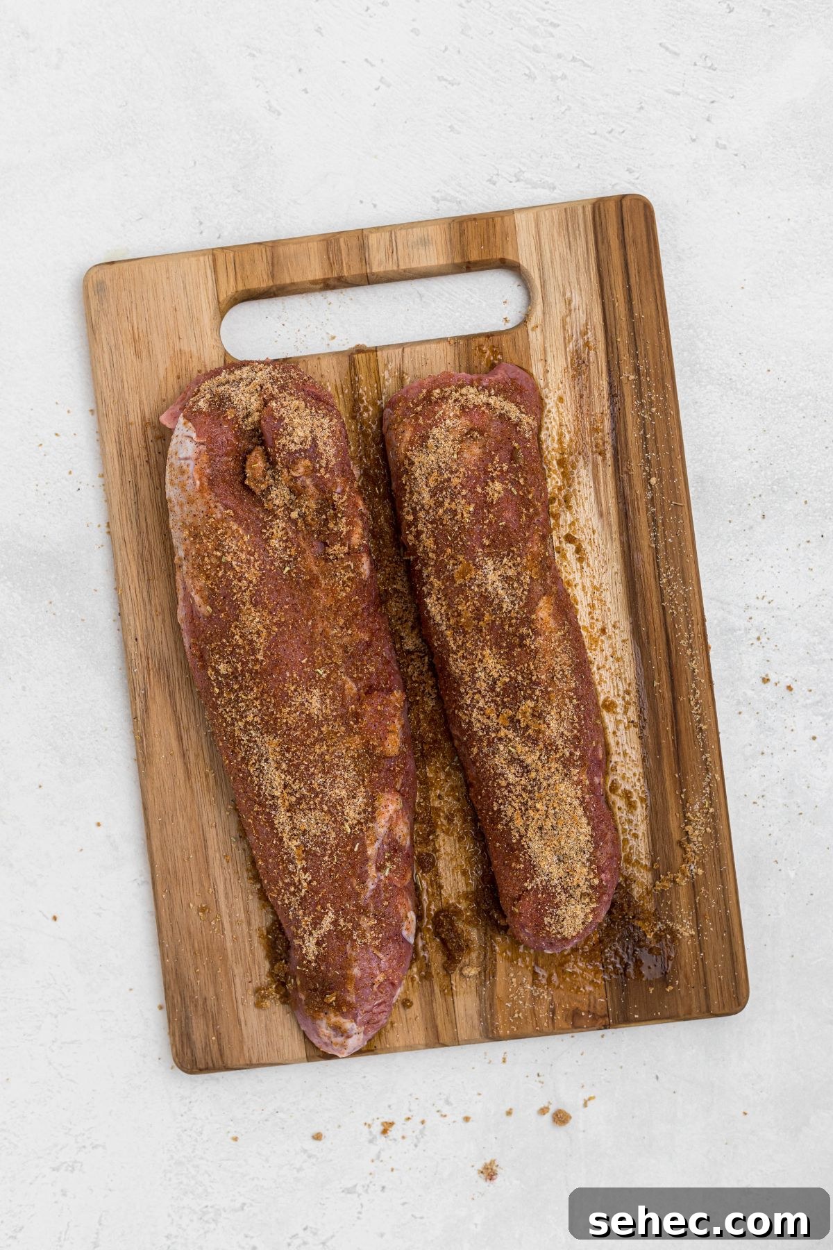 Juicy Smoked Pork Tenderloin Recipe 6 Uncooked, seasoned pork tenderloins on wooden cutting board.