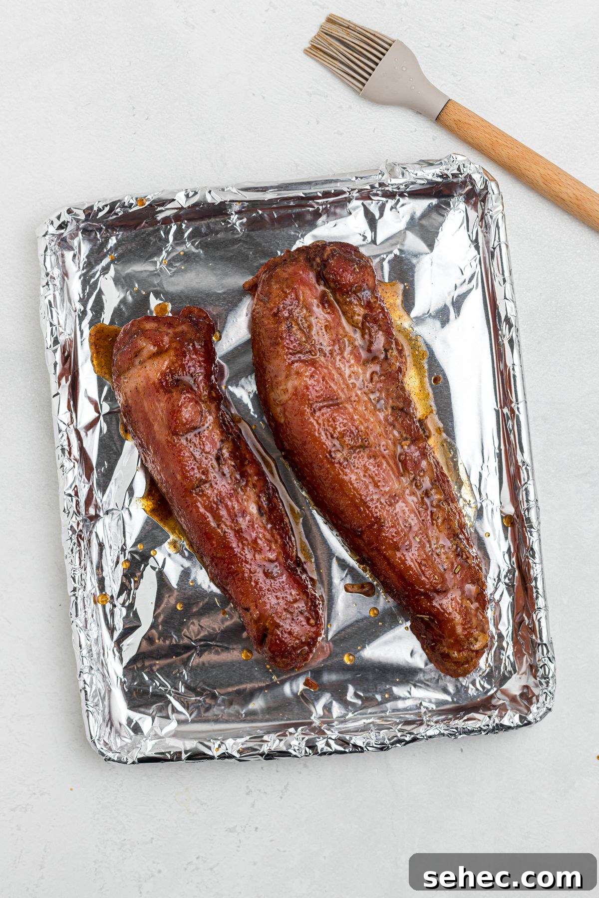 Juicy Smoked Pork Tenderloin Recipe 8 Juicy smoked tenderloins on foil covered baking sheet after being brushed with honey glaze.