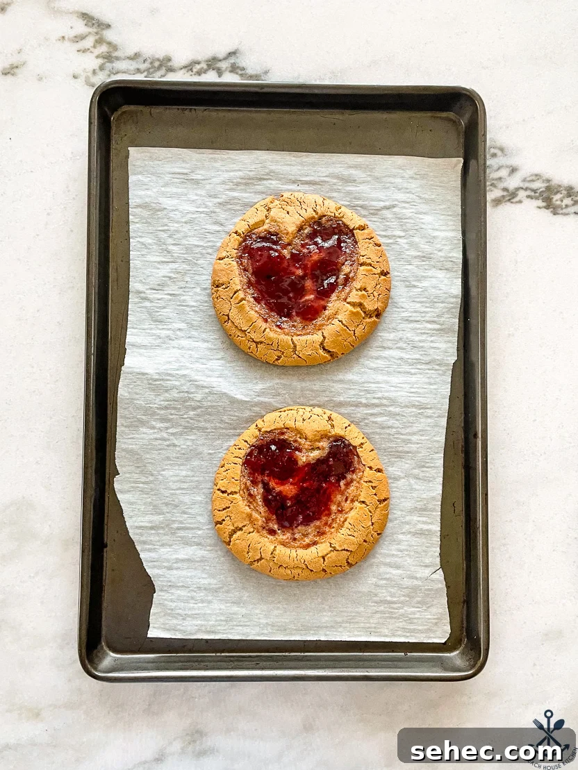 Giant Peanut Butter and Jelly Cookies for Two 3 Overhead photo of a baking sheet with two large peanut butter cookies with jelly heart indent.