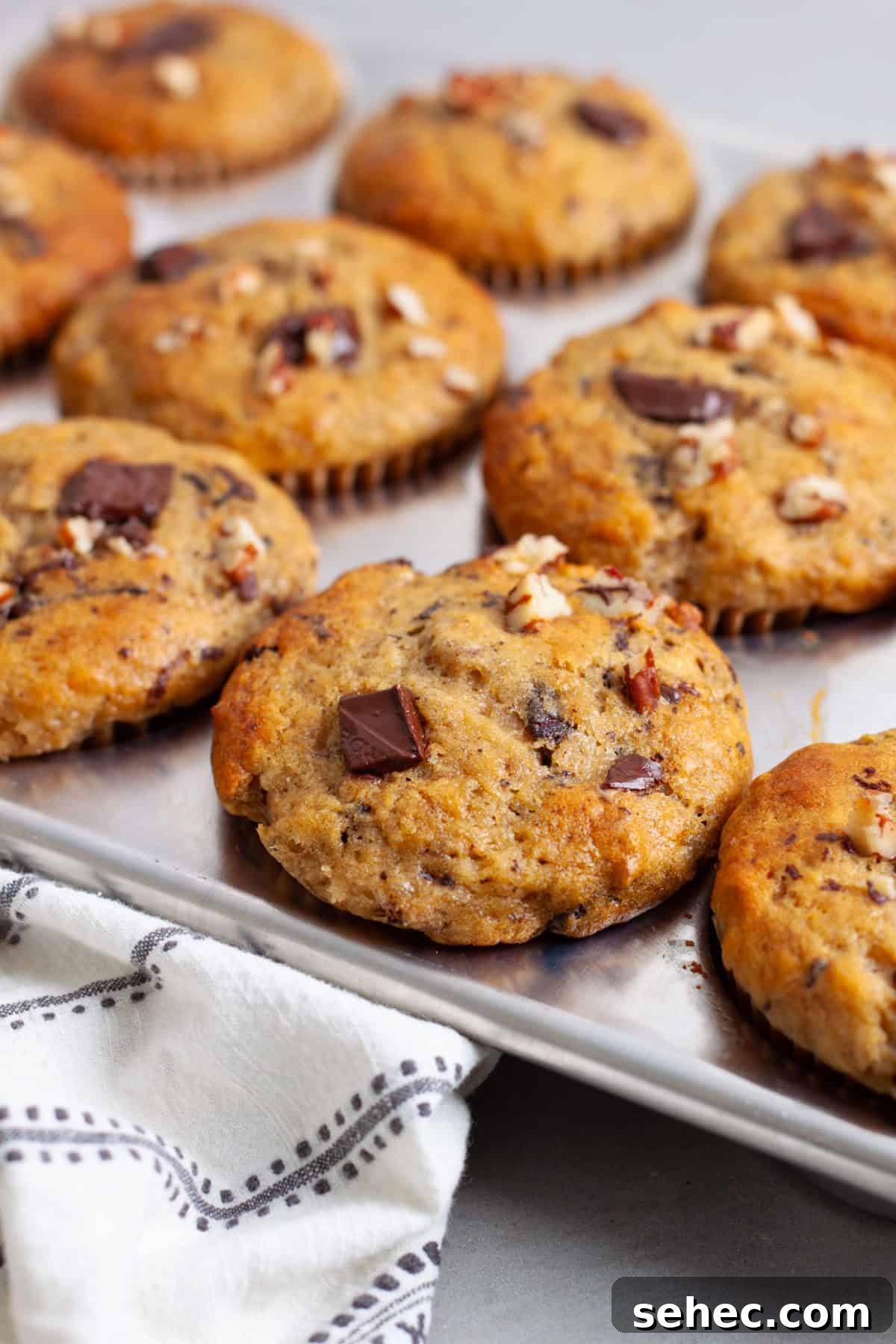 Moist Banana Chocolate Chunk Muffins 2 A muffin tin with golden brown banana chocolate chunk muffins on a gray table.