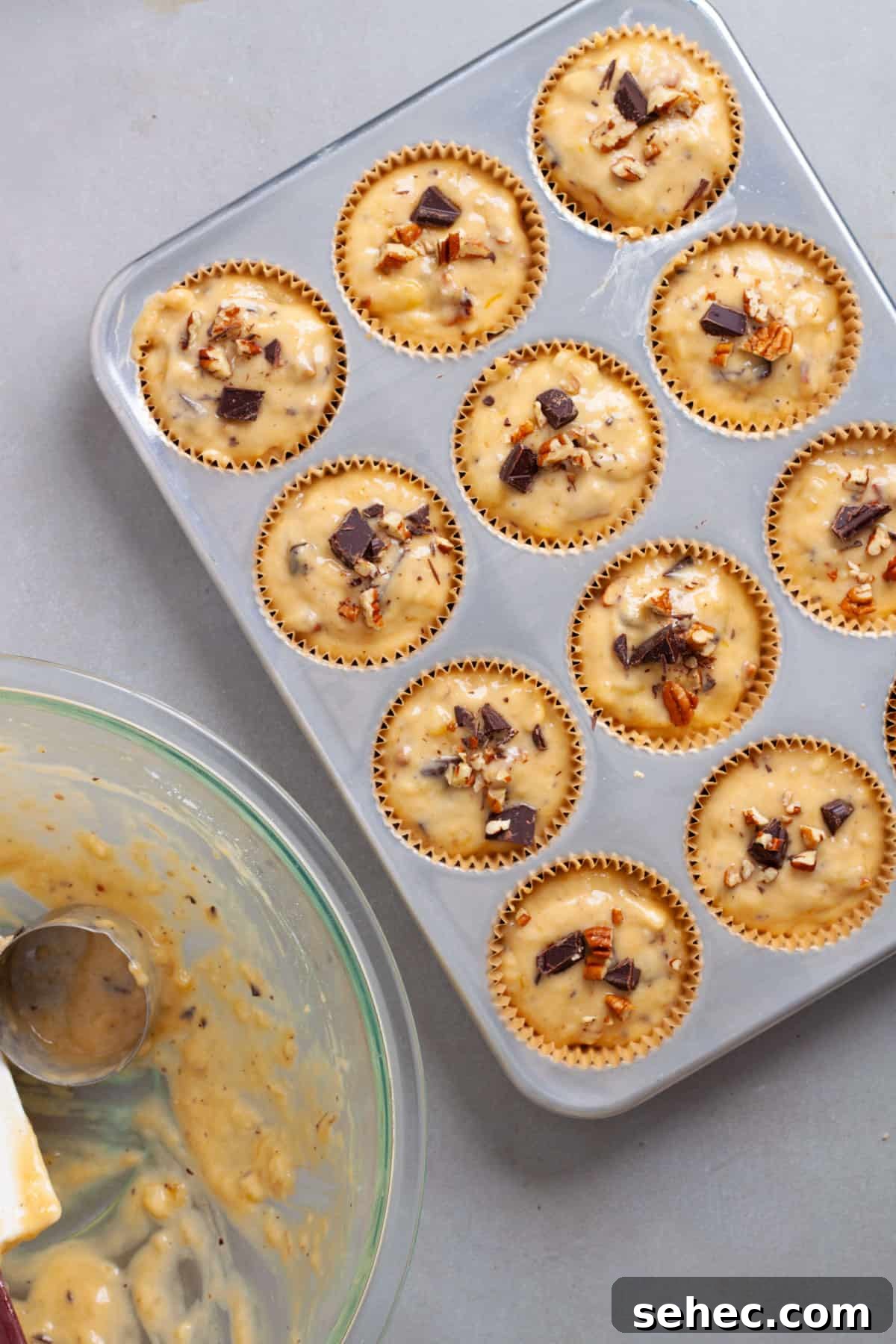 Moist Banana Chocolate Chunk Muffins 10 Banana chocolate muffin batter added to a muffin tin and topped with chopped pecans.