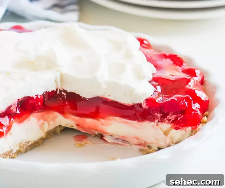 Cherry Cream Pie Recipe with Flaky Crust 6 sliced cherry cream pie in a pie plate with plates and a striped dish towel in the background