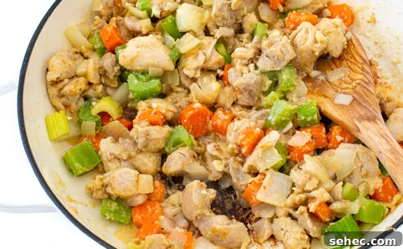 Slow Cooker Chicken Stew with Vegetables 6 The stew mixture in a white skillet with a wooden spoon stirring it.