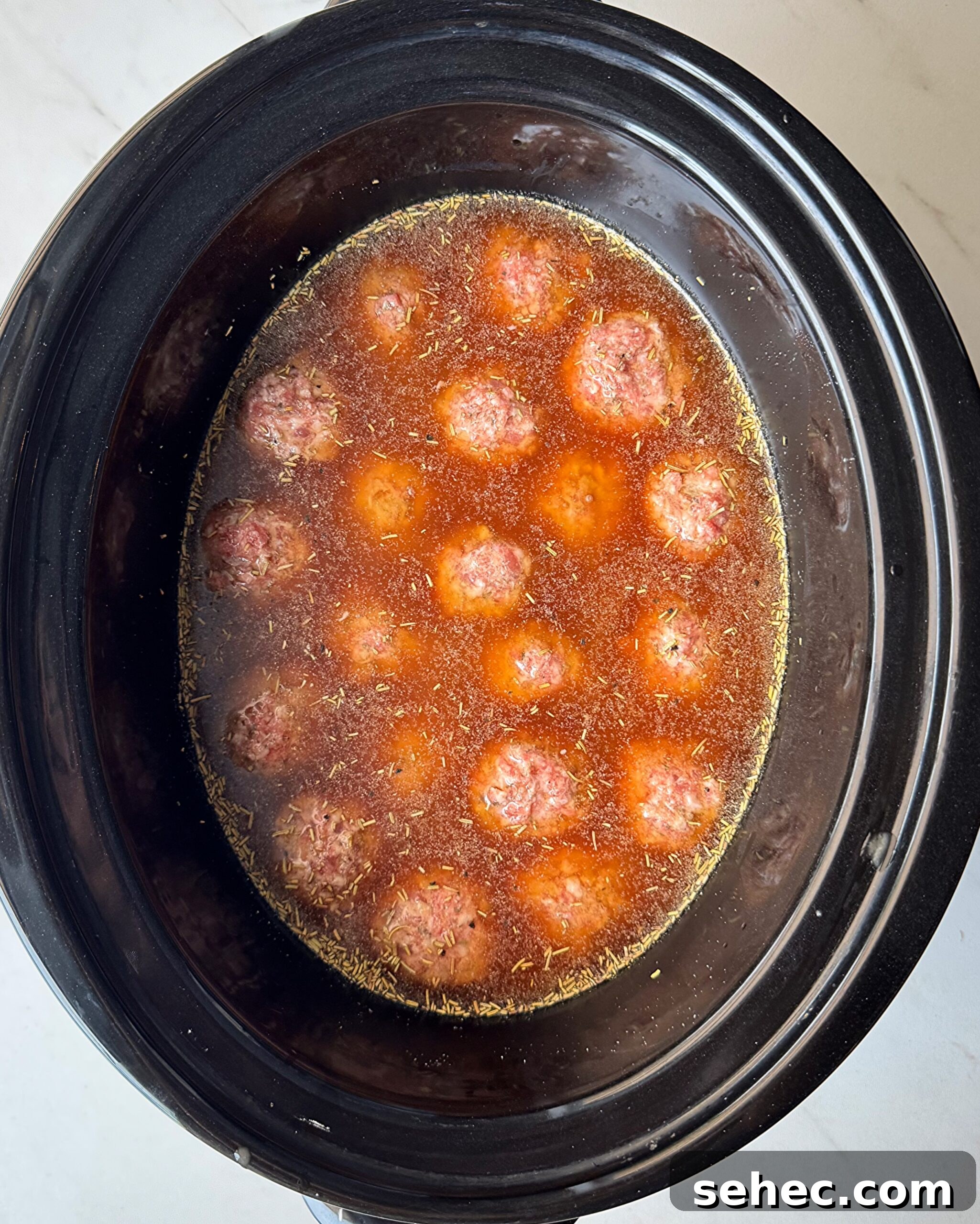 overhead shot of uncooked meatballs and gravy in a black slow cooker