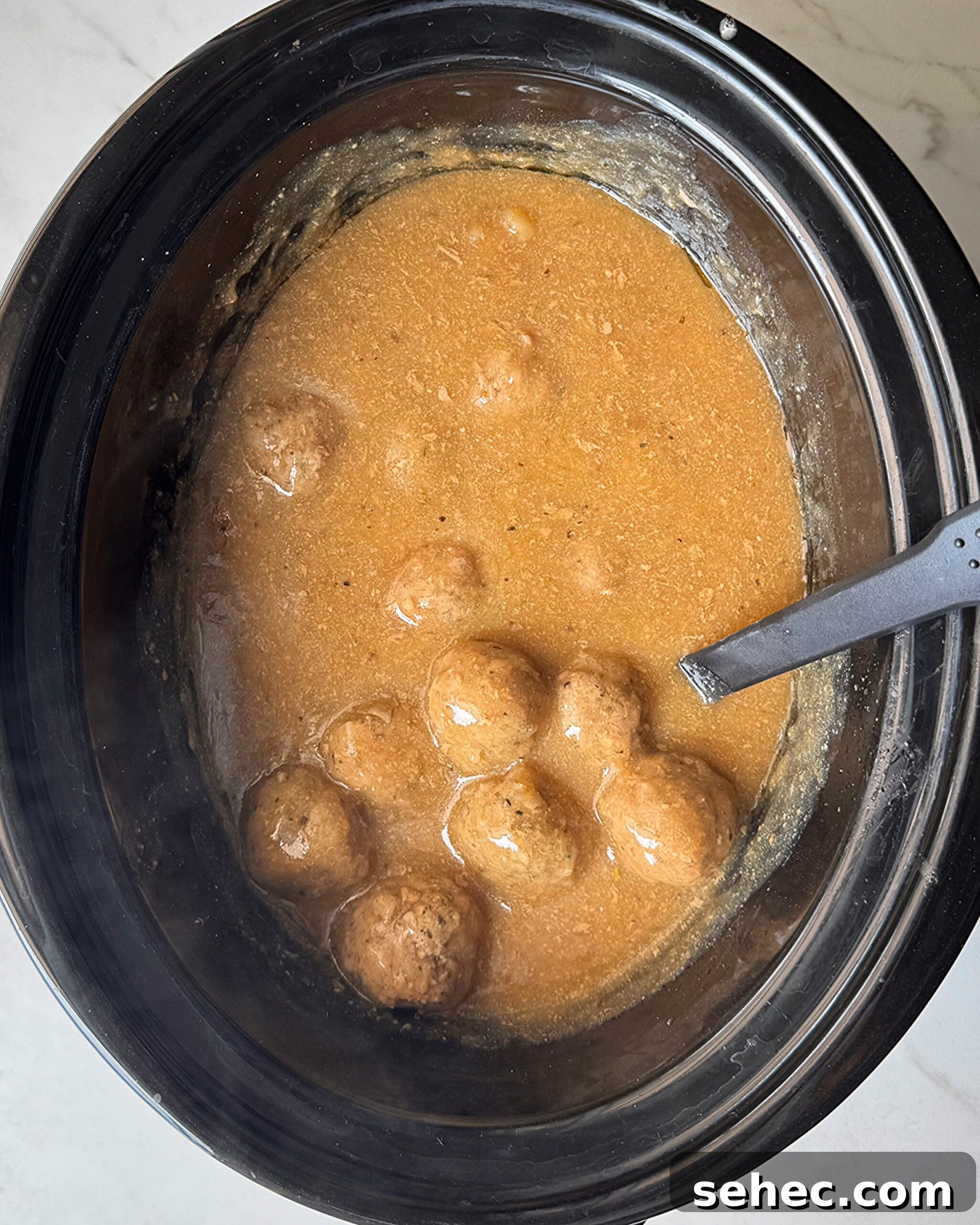 overhead shot of cooked meatballs and gravy in a black slow cooker