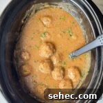 overhead shot of cooked meatballs and gravy in a black slow cooker garnished with fresh parsley