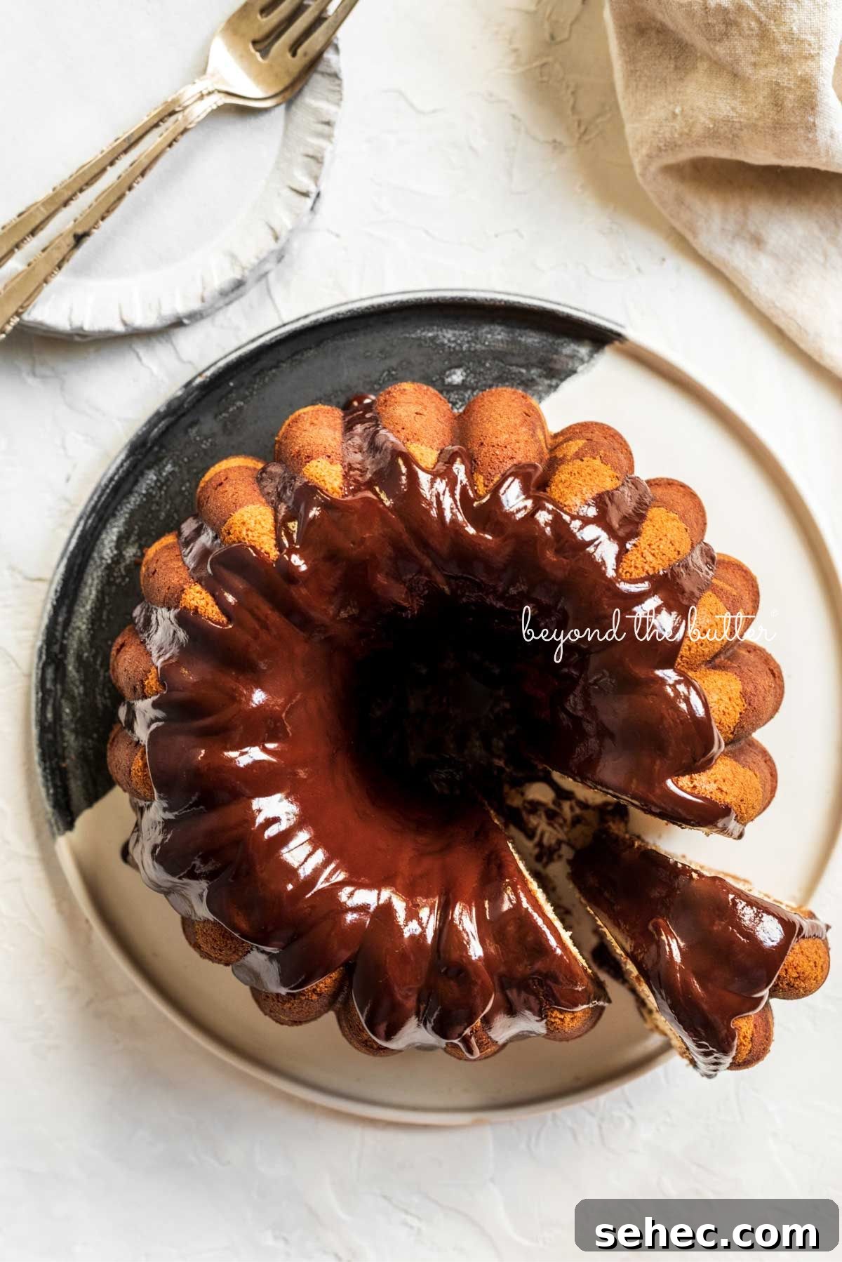 Moist Marble Bundt Cake Recipe 15 Marble bundt cake on a black and white ceramic dessert plate with chocolate ganache glaze drizzled over the top with a a slice partially removed.