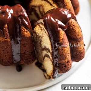 Moist Marble Bundt Cake Recipe 20 Chocolate glazed marble bundt cake with one slice partially removed on a white ceramic dessert plate and white background.