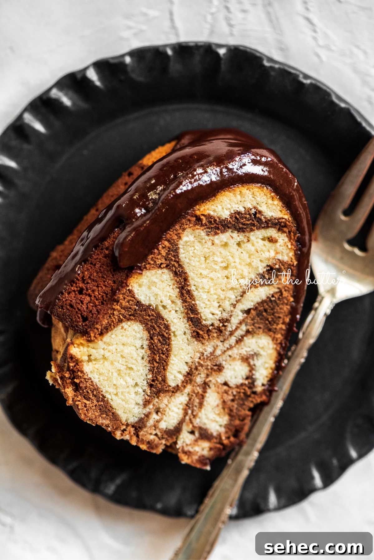 Moist Marble Bundt Cake Recipe 3 Slice of marble bundt cake on black dessert plate with fork placed next to it on a white background.