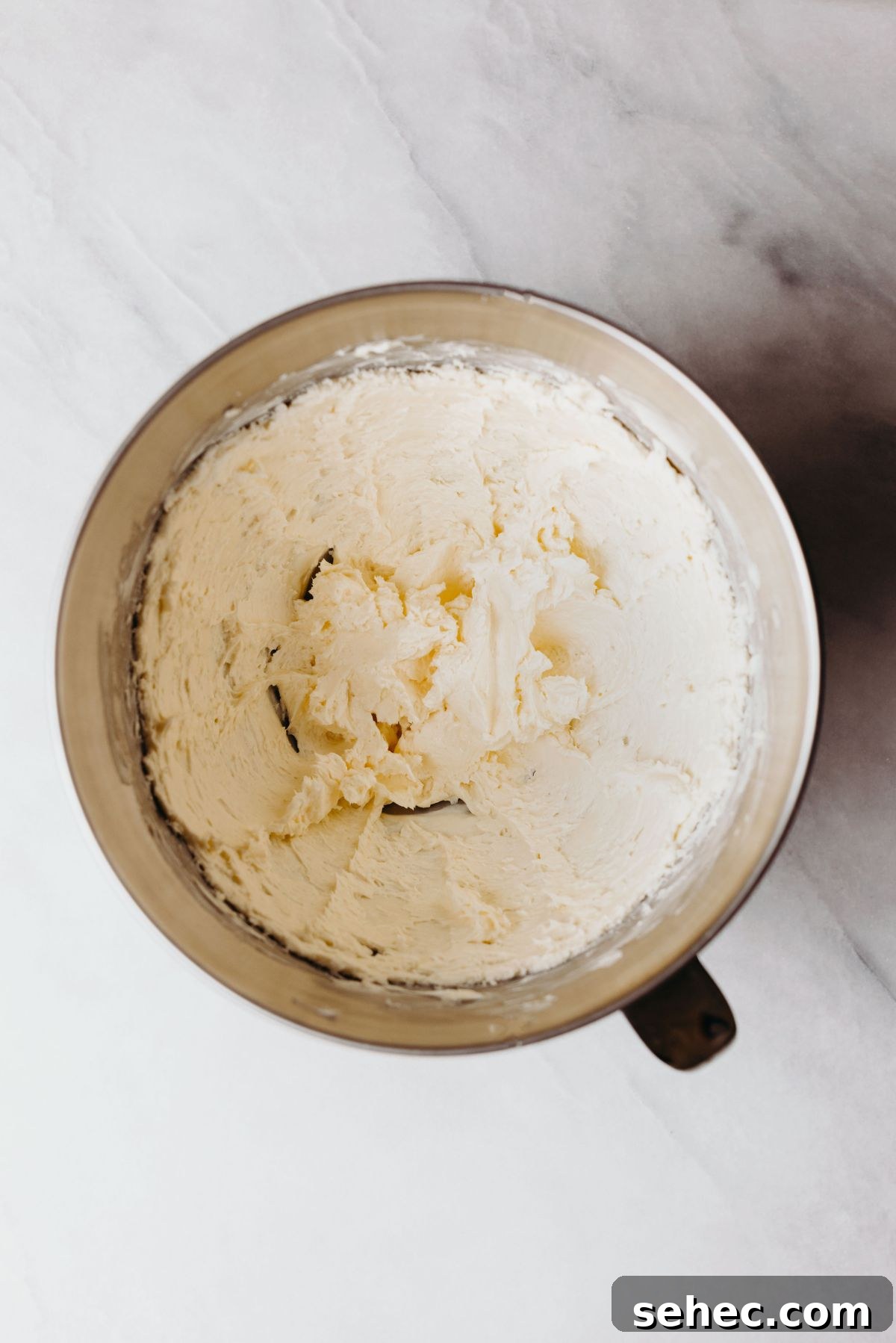 Moist Marble Bundt Cake Recipe 5 Beaten cream cheese and unsalted butter in a stainless steel mixing bowl on a white marbled background.