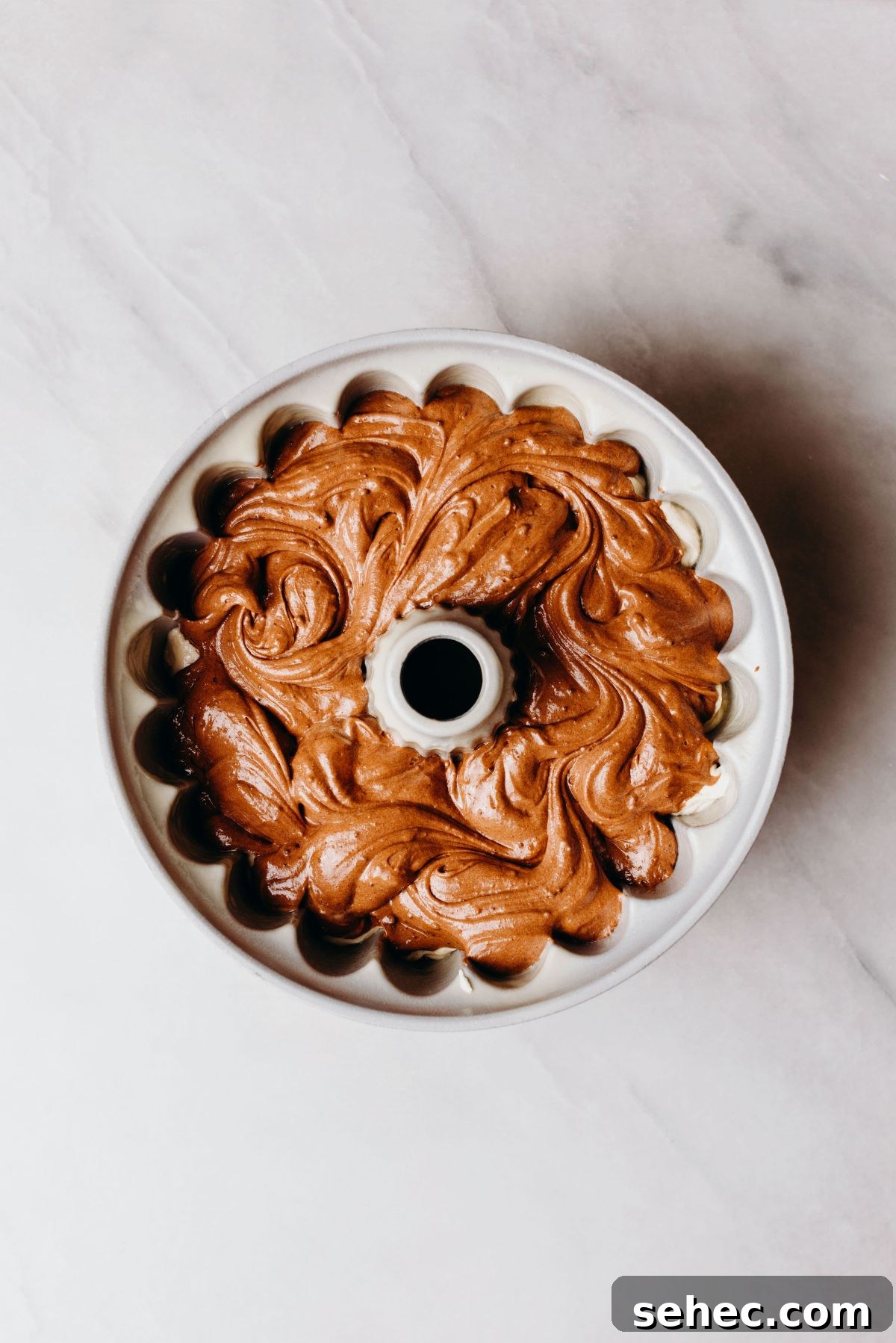 Moist Marble Bundt Cake Recipe 10 Swirled chocolate and vanilla cake batter in a bundt cake pan on a white marbled background.