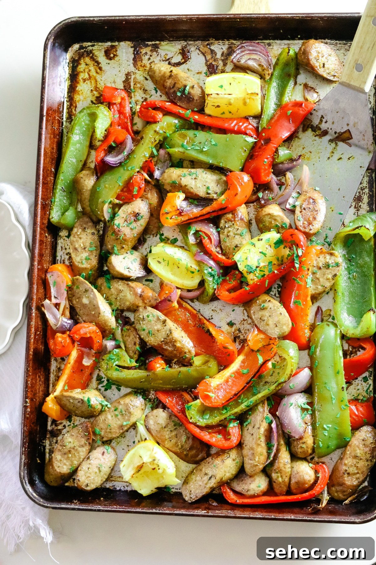 Oven Baked Sausage and Peppers Recipe 2 Sausage and peppers on a baking sheet, with two white plates on the side.