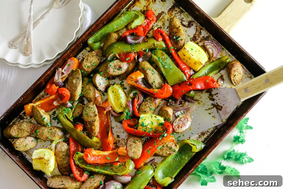 Oven Baked Sausage and Peppers Recipe 14 Sausage and peppers on a baking sheet, with two white plates and utensils on the side.