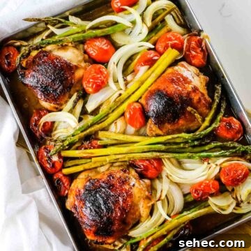 golden brown balsamic chicken roasted on sheet pan with asparagus, tomatoes, and onions.
