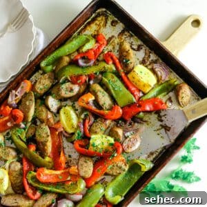 Oven Baked Sausage and Peppers Recipe 19 Sausage and peppers on a baking sheet, with two white plates and utensils on the side.