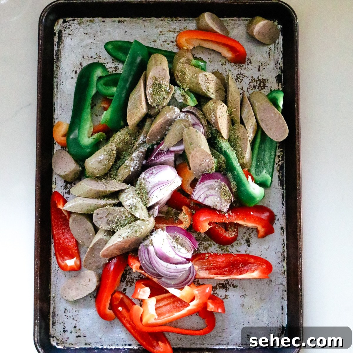 Oven Baked Sausage and Peppers Recipe 6 Sausage and peppers with seasoning on a baking sheet.