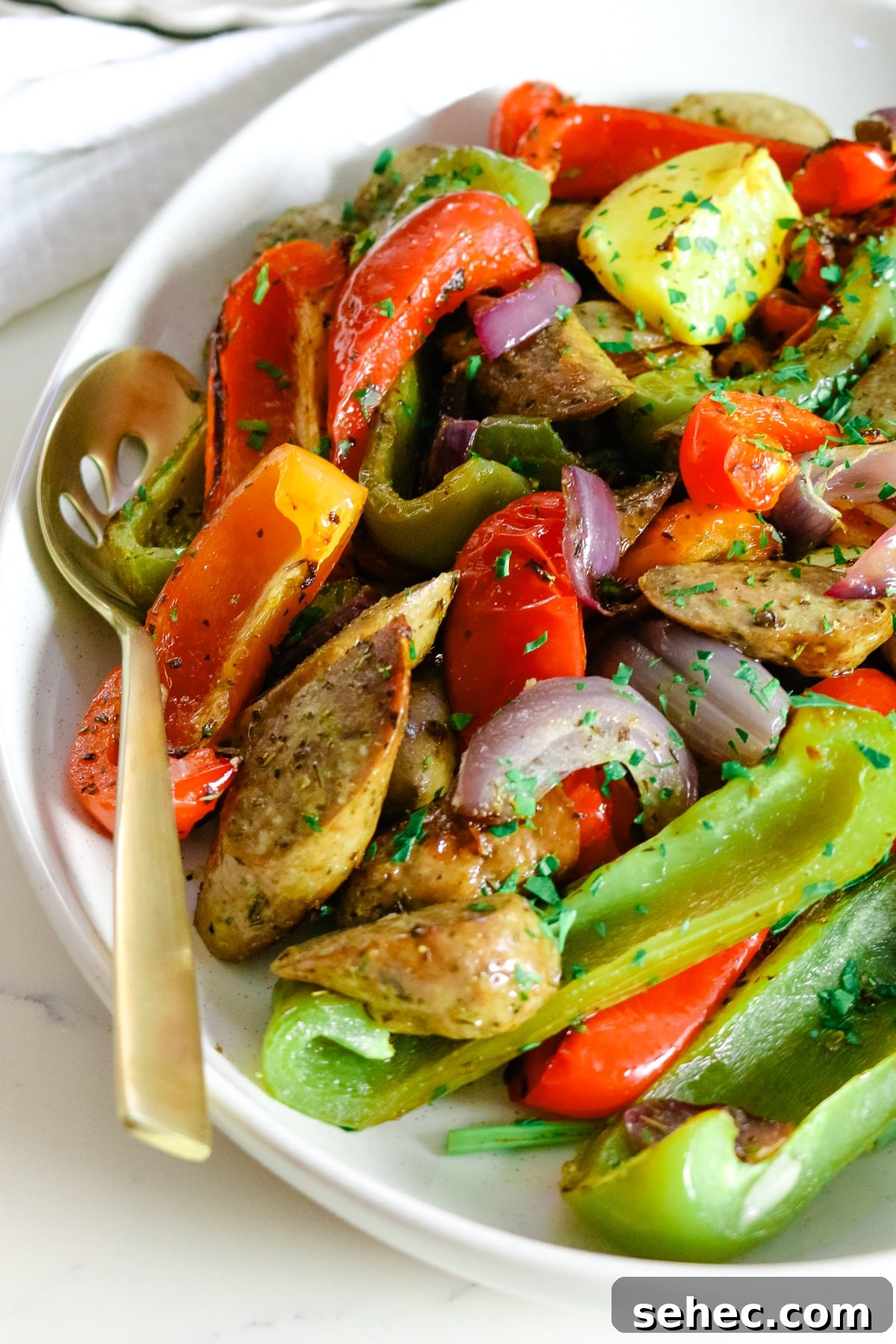 Oven Baked Sausage and Peppers Recipe 9 Sausage and peppers on a white plate, with a spoon in it.