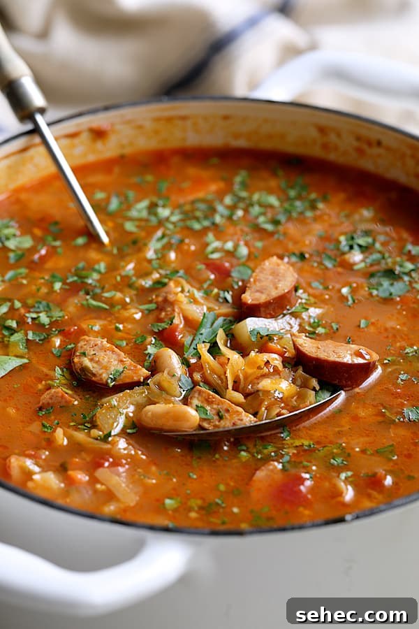 Farmhouse Kielbasa Cabbage Soup with Cannellini Beans 4 Close-up photo of Farmhouse Cabbage Soup with Cannellini Beans and Kielbasa in white Dutch oven.