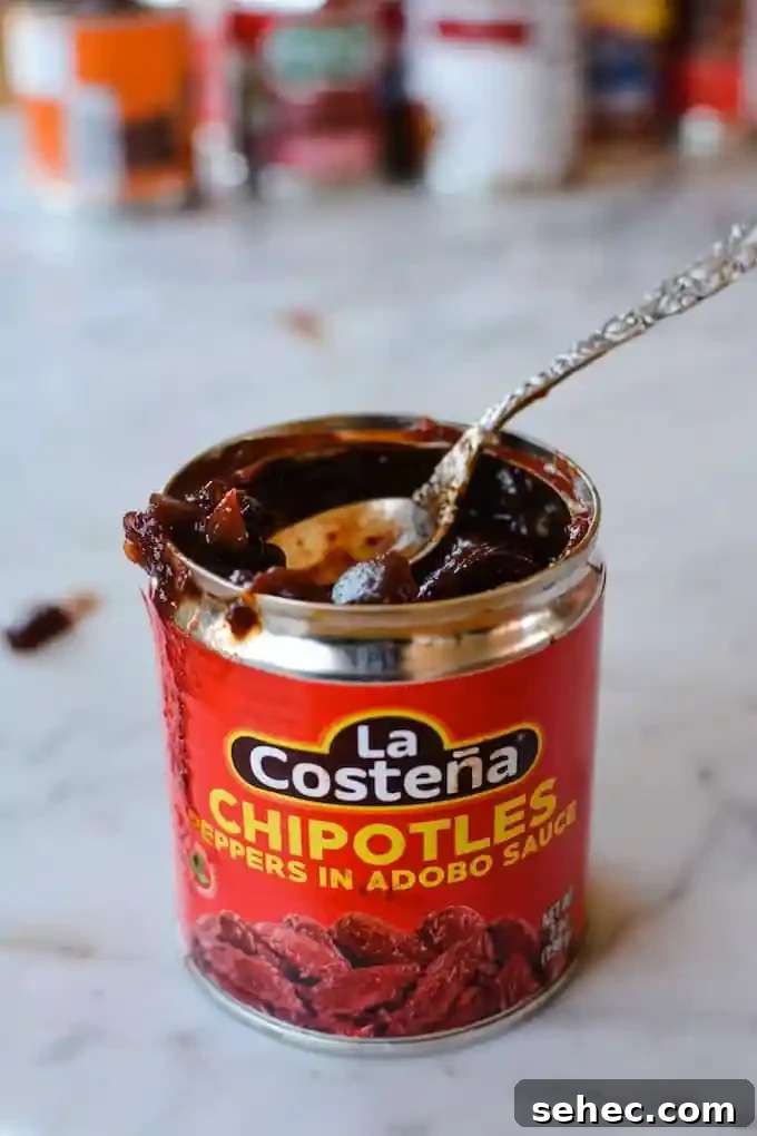 Over 35 Recipes Using Canned Chipotle Peppers in Adobo 4 A can of chipotle in adobo sauce that is open with a spoon dipped into the can sitting on a marble table.
