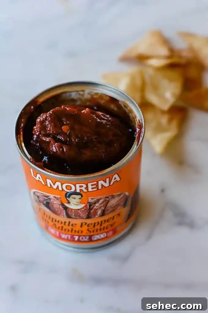 Over 35 Recipes Using Canned Chipotle Peppers in Adobo 5 An orange can of chipotle in adobo sauce opened on a marble counter with a pile of tortilla chips behind it.