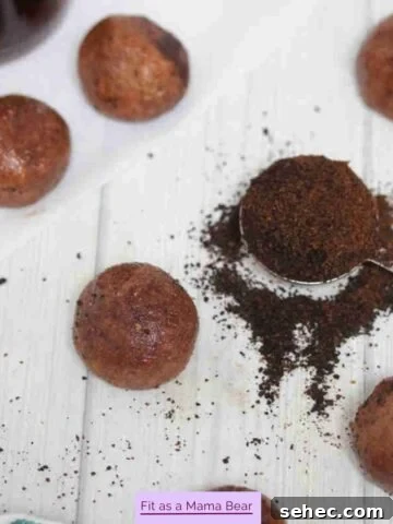 Coffee protein balls covered in cocoa powder with a spoon of coffee grinds beside them.