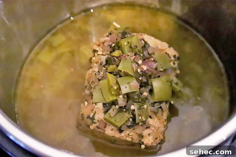 Slow Cooker Pork Tacos for Taco Tuesday 9 Horizontal image of a cooked slab of meat in juices and cooked peppers and onions.