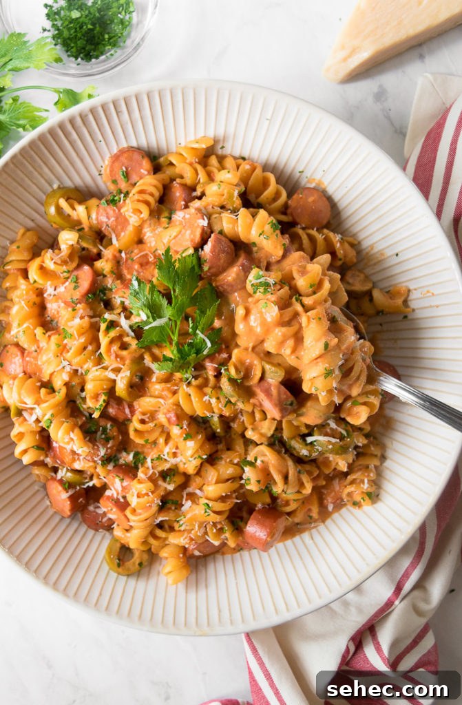 Creamy Hot Dog Pasta Recipe with Tomato Sauce 2 a white bowl holds hot dog pasta and a fork in it, garnished with parsley