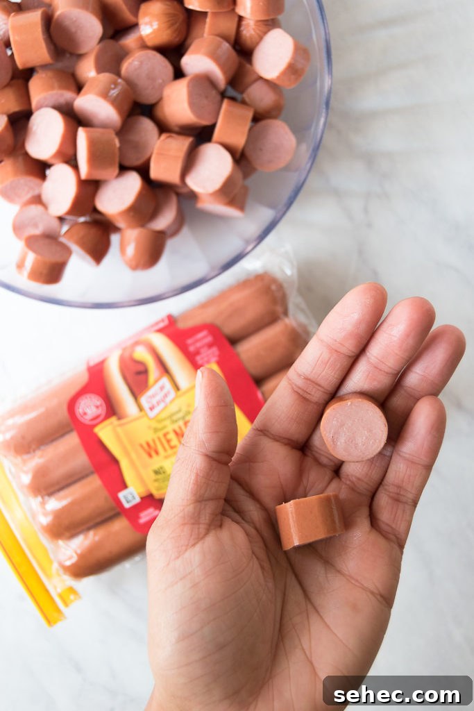 Creamy Hot Dog Pasta Recipe with Tomato Sauce 4 a hand holds sliced, bite-sized hot dog pieces over a package of hot dogs on a marble surface
