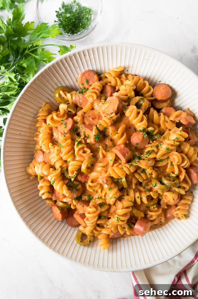Creamy Hot Dog Pasta Recipe with Tomato Sauce 9 a white bowl of hot dog pasta with rotini on a white surface garnished with fresh parsley
