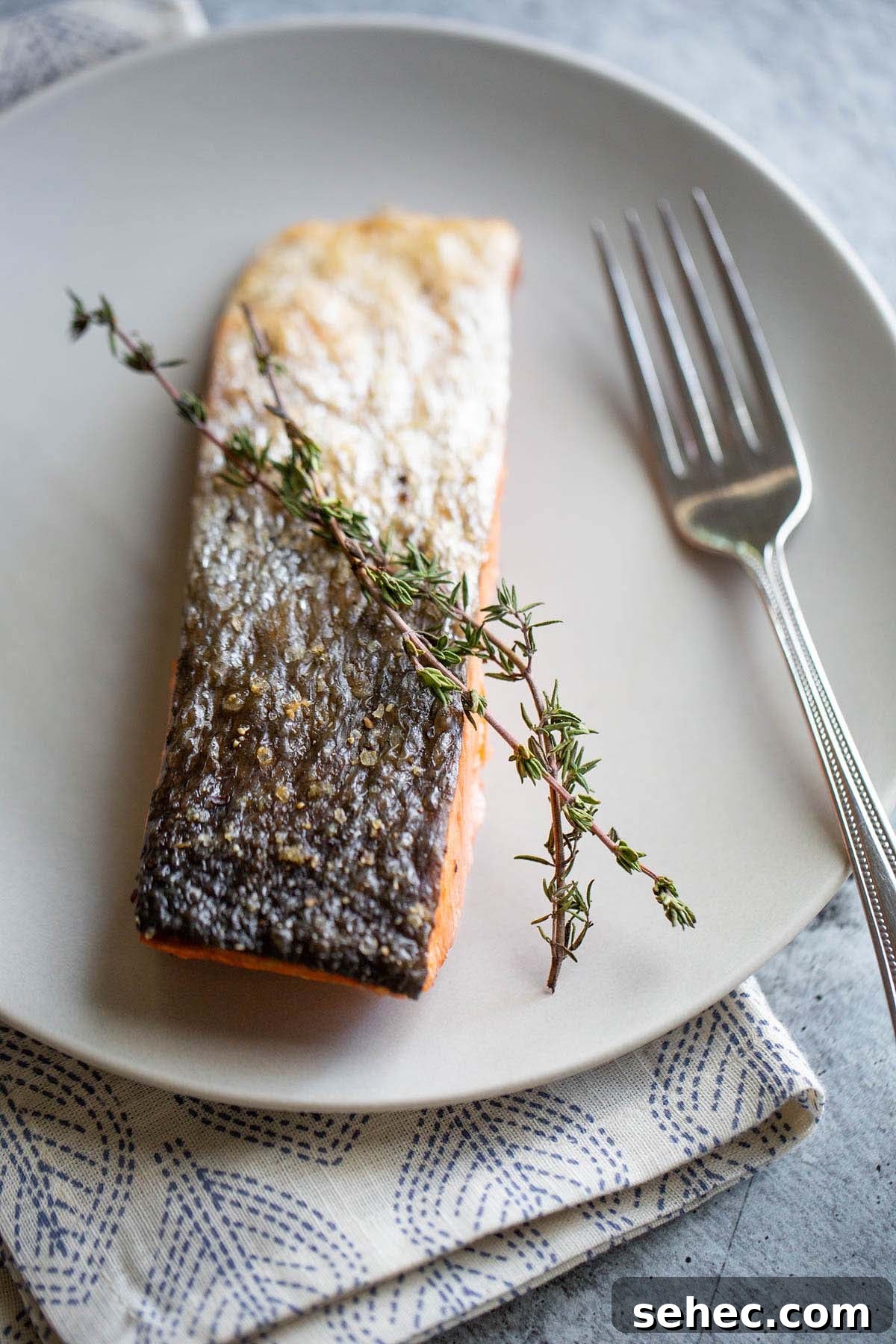 Crispy Skin Air Fryer Salmon Recipe 8 Salmon on a plate with a sprig of fresh thyme.
