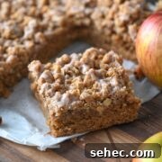 Moist Applesauce Crumb Cake with Cinnamon Streusel 8 slice of moist applesauce crumb cake on parchment paper next to the rest of the cake and fresh apples.
